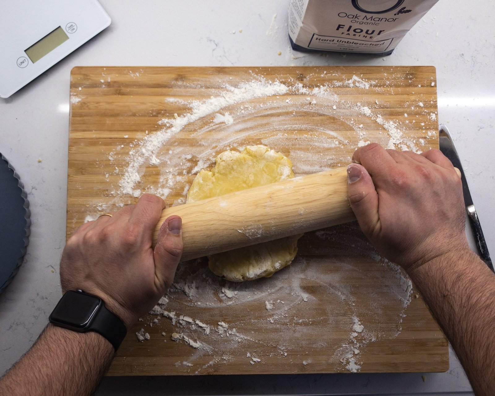 Pastry being rolled out with a rolling pin on a wooden surface