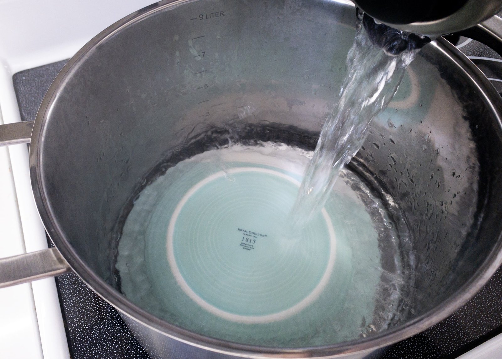 An upturned plate in a large stock pot being filled with water