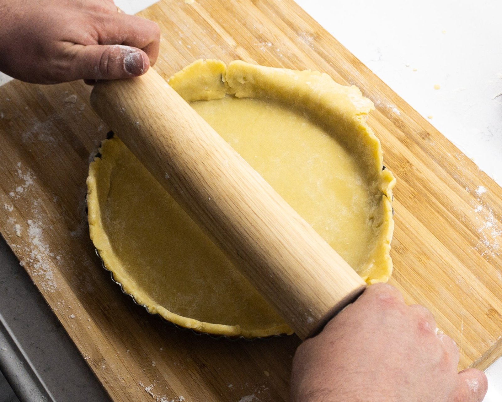 Rolling pin being used to cut the excess pastry from a tart tin